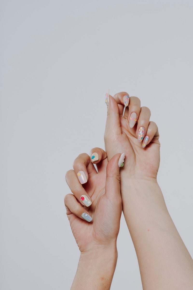 Long oval acrylic nails finished in pearlescent pastel tones with delicate dotted accents and confetti glitter art