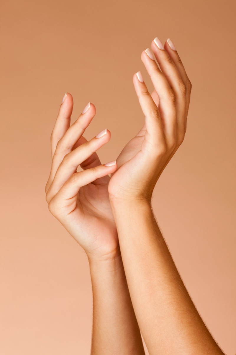 Two hands lifted gracefully against a warm tan backdrop, showing a clean glossy French finish on a builder gel overlay