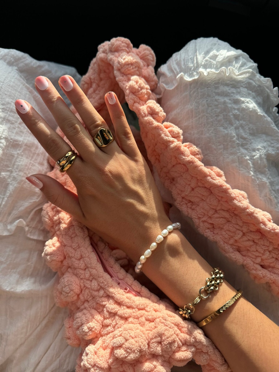 A hand resting on a soft pink chunky knit blanket, fingers tipped with a clean Gel X French manicure on a sunny afternoon