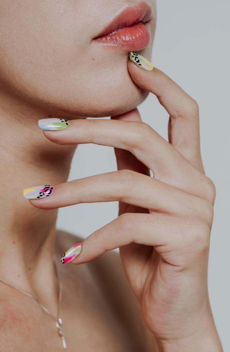 Close-up of a model with vibrant abstract SNS nail art — pinks, yellows, greens and leopard-print accents — resting against the chin